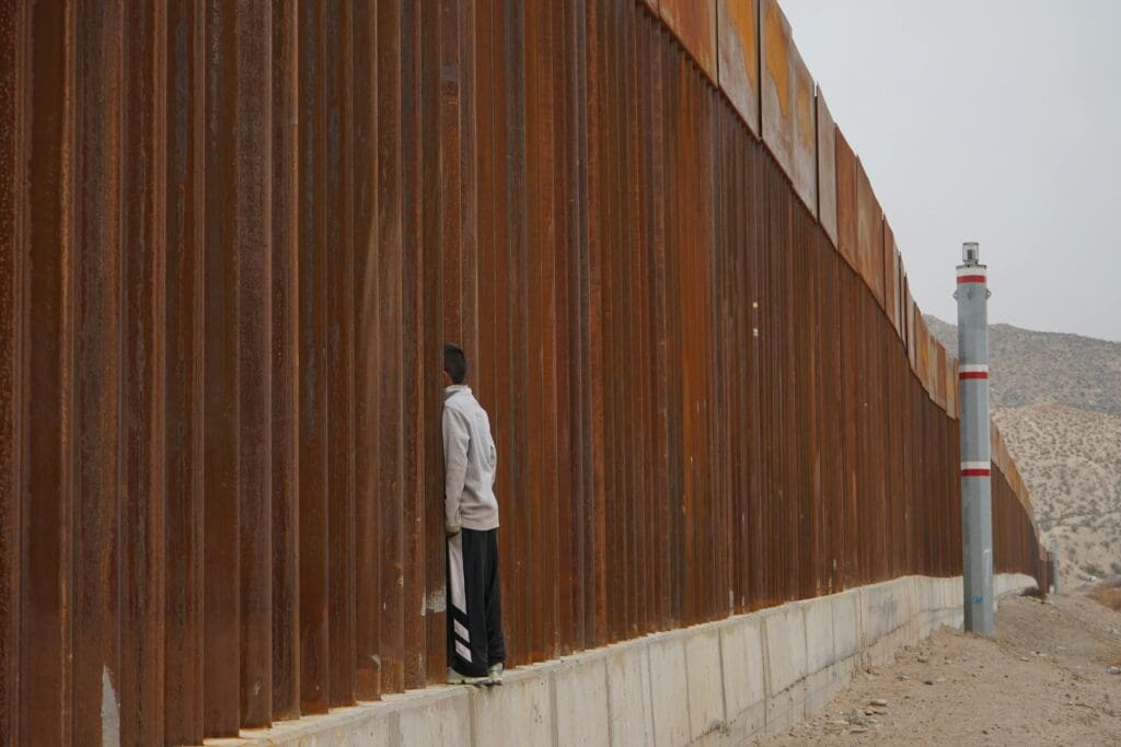 A person standing near a tall, rust-colored metal fence.