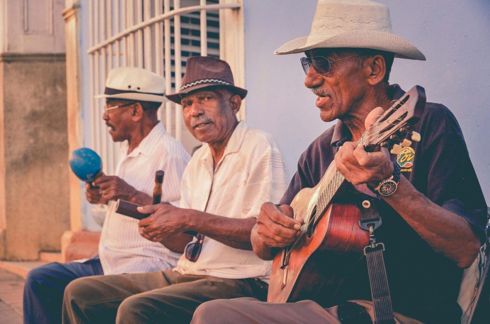 Three elderly men playing string instruments outdoors, enjoying music together.