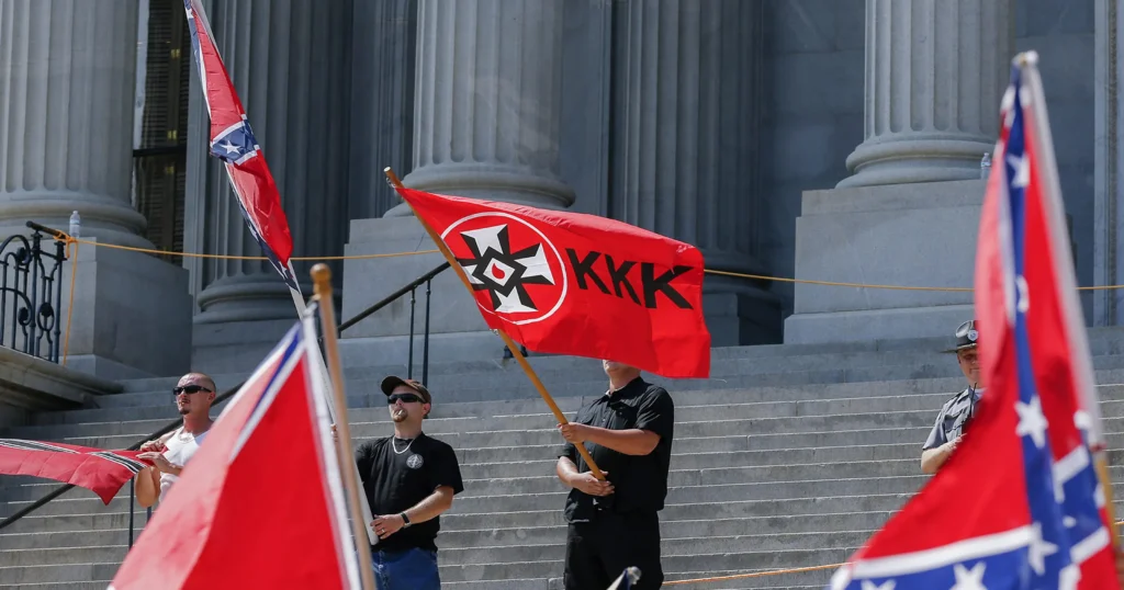 Individuals holding a KKK flag during a public event.