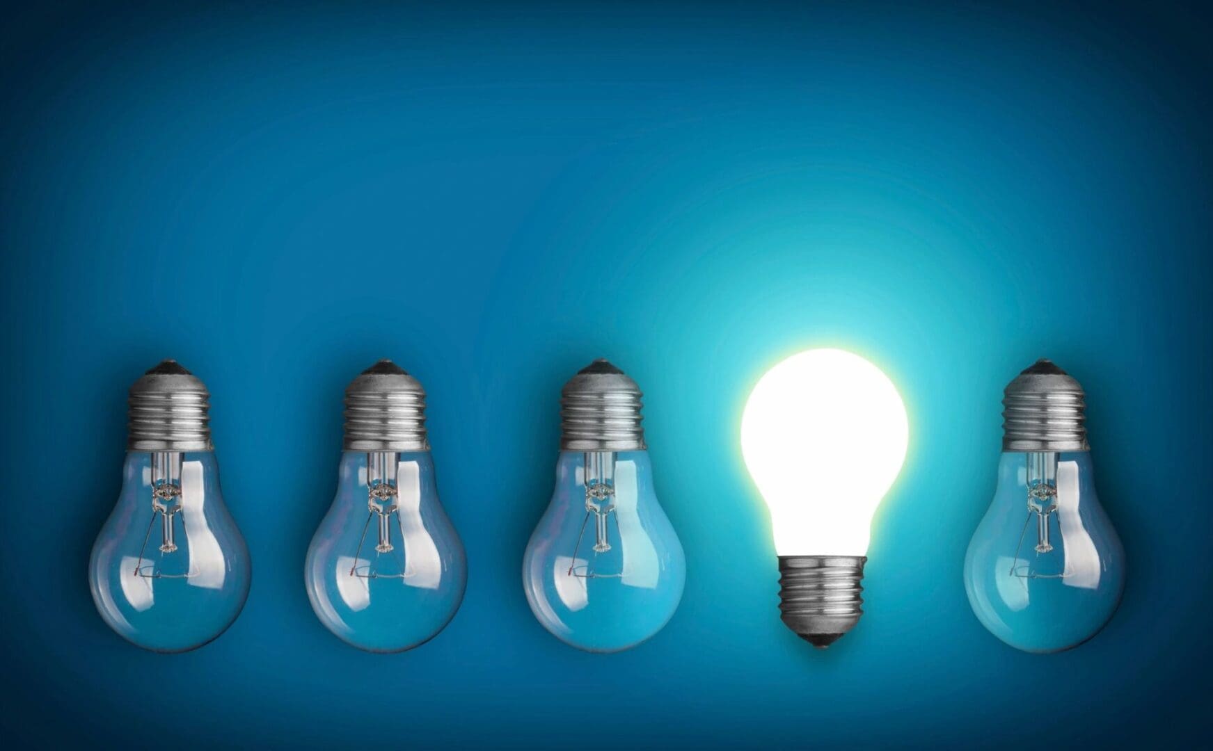 One light bulb glowing among three unlit bulbs against a blue background.