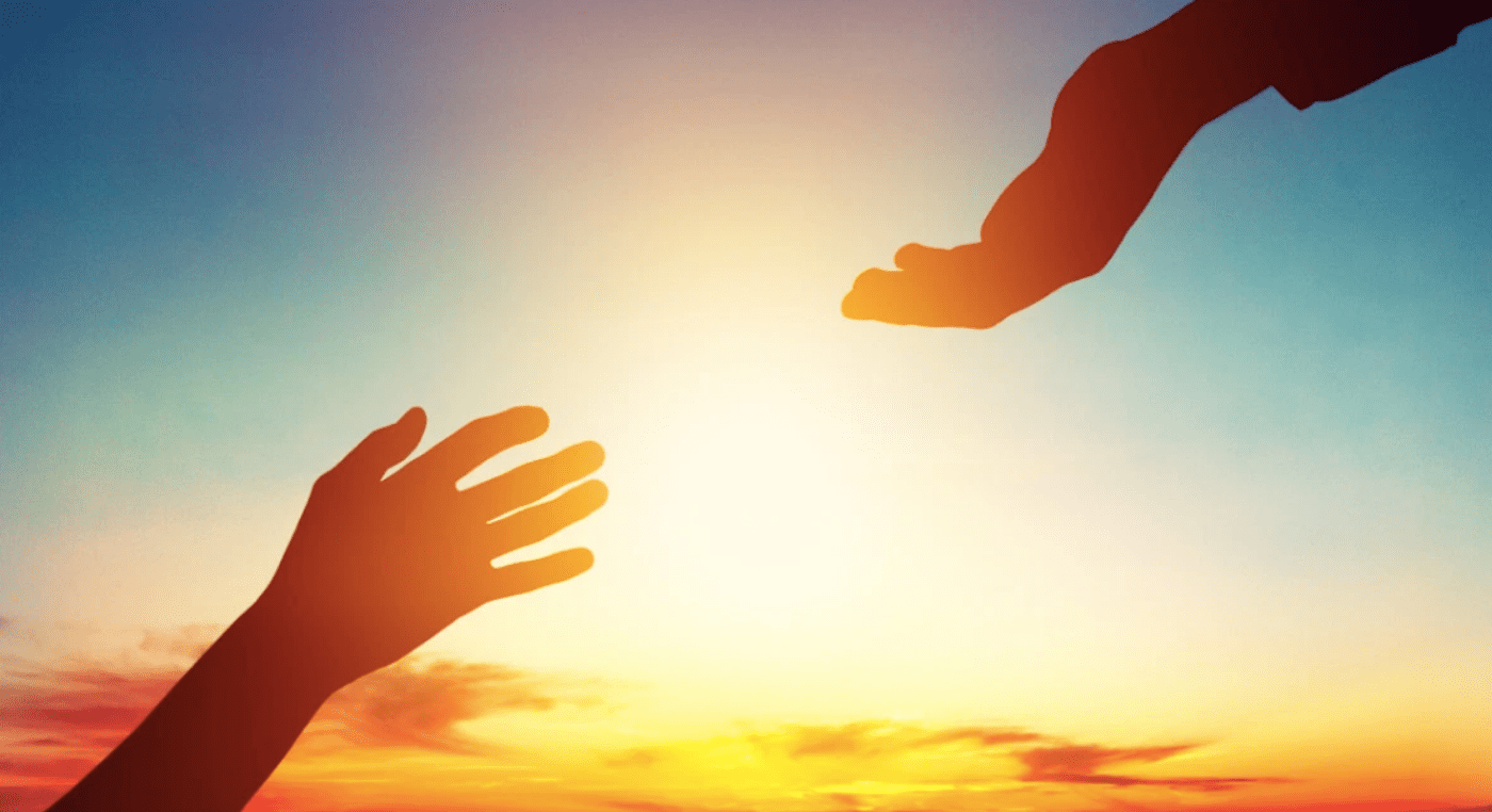 Two hands reaching out against a sunset sky.