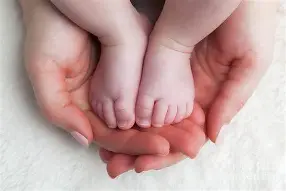 Adult hands gently holding a baby's feet.