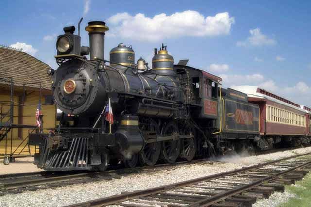A vintage steam locomotive train on railroad tracks under a blue sky.