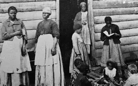 Historical photo of African American women and children outside a wooden building.