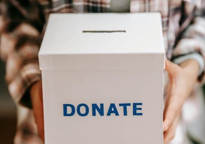 Person holding a white donation box labeled 'DONATE'.